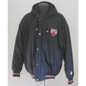 May include: Black Chicago Bulls hooded jacket with snap closures and a red, white, and black Bulls logo on the chest. The jacket has a hood, a red and white striped hem and cuffs, and the Starter logo.