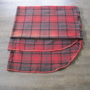 May include: A red and black plaid blanket with a rounded edge. The blanket is folded in half and has a subtle ombre effect.