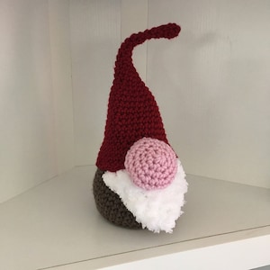 May include: A crocheted gnome with a red hat, brown body, white beard, and pink nose.
