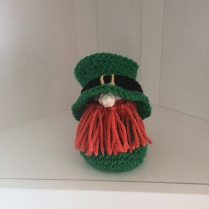 Könnte beinhalten: Ein grüner, gehäkelter Leprechaun-Zwerg mit einem schwarzen Hut und einem roten Wollbart.