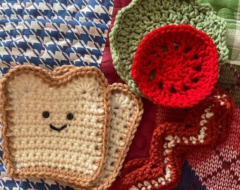 May include: A set of crocheted food items including two slices of beige bread with brown crusts and embroidered black faces, a round green lettuce leaf, a round red tomato slice, and a wavy strip of brown and white bacon made of yarn.