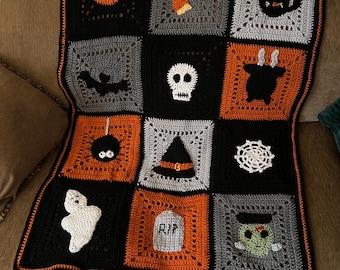 May include: A handmade crochet blanket featuring a grid of twelve square panels in black, orange, and gray. The squares display Halloween-themed motifs including a pumpkin, black cat, bat, skull, spider, witch hat, spiderweb, ghost, and tombstone with RIP.