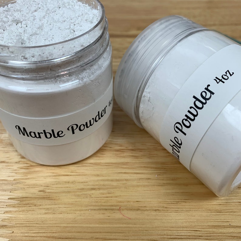 Peut inclure: Deux pots en plastique transparent remplis de poudre de marbre blanche. Les pots portent des &eacute;tiquettes noires indiquant "Marble Powder" et "4 oz".