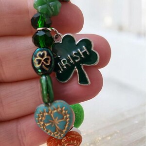 Könnte beinhalten: Ein grünes und blaues Charm-Armband mit einem Kleeblatt-Anhänger, auf dem "IRISH" steht.