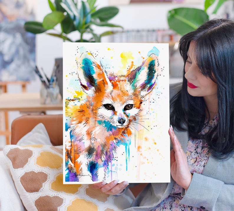 Puede incluir: Pintura acuarela de un zorro fennec con pelaje naranja, orejas grandes y ojos negros. La pintura tiene un fondo colorido con salpicaduras de amarillo, azul y morado.