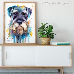 Op de afbeelding: Waterverf schilderij van een zwarte en grijze Schnauzer hond met blauwe, gele en oranje waterverf accenten. Het schilderij is ingelijst en hangt aan een muur boven een witte kast.
