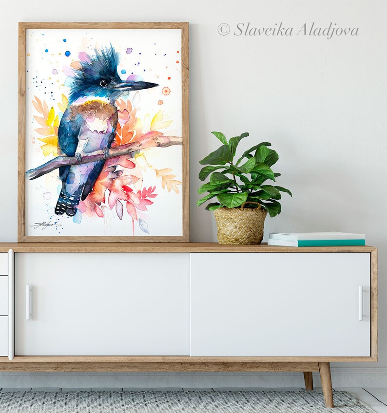 May include: Watercolor painting of a blue and brown kingfisher bird perched on a branch with colorful leaves and a white background.