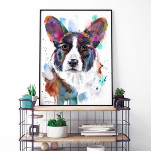 Op de afbeelding: Waterverf schilderij van een Cardigan Welsh Corgi hond met bruin, zwart en wit haar. De ogen van de hond zijn bruin en de achtergrond is lichtblauw met kleurspatten.