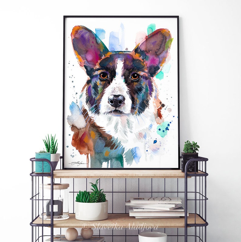 Op de afbeelding: Waterverf schilderij van een Cardigan Welsh Corgi hond met bruin, zwart en wit haar. De ogen van de hond zijn bruin en de achtergrond is lichtblauw met kleurspatten.