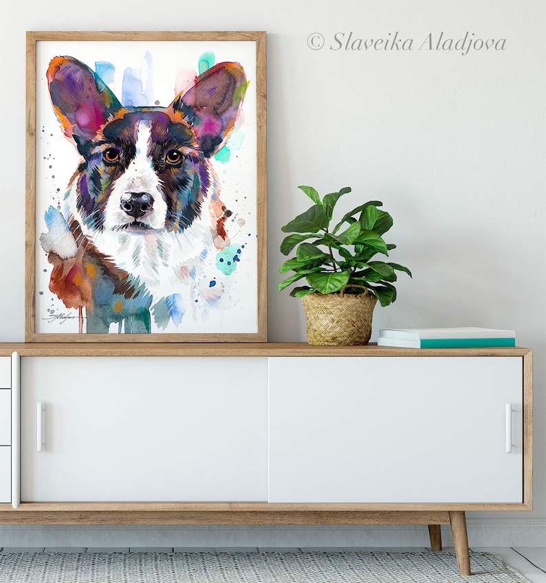 Op de afbeelding: Waterverf schilderij van een Cardigan Welsh Corgi hond met bruine, witte en paarse vacht. De hond kijkt recht naar de kijker. De achtergrond is lichtblauw met spatten van kleur.