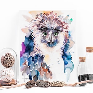 May include: Watercolor painting of a Philippine eagle with green eyes, brown and white feathers, and a blue and purple background.