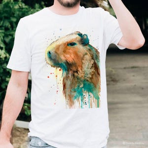 May include: A white t-shirt with a watercolor illustration of a capybara. The capybara is brown with splashes of blue and green paint.