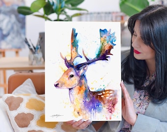 Puede incluir: Pintura acuarela de un ciervo con grandes cuernos. El ciervo está pintado en tonos de morado, azul, amarillo y marrón. El fondo es blanco con salpicaduras de color.