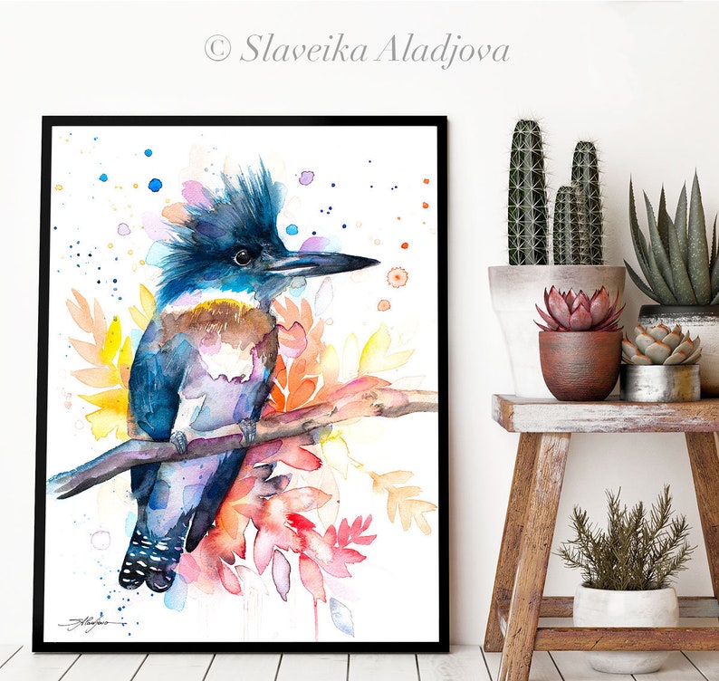 May include: Watercolor painting of a blue and brown kingfisher perched on a branch with colorful flowers. The bird has a crest of feathers and a long beak. The background is white with scattered blue and pink dots.