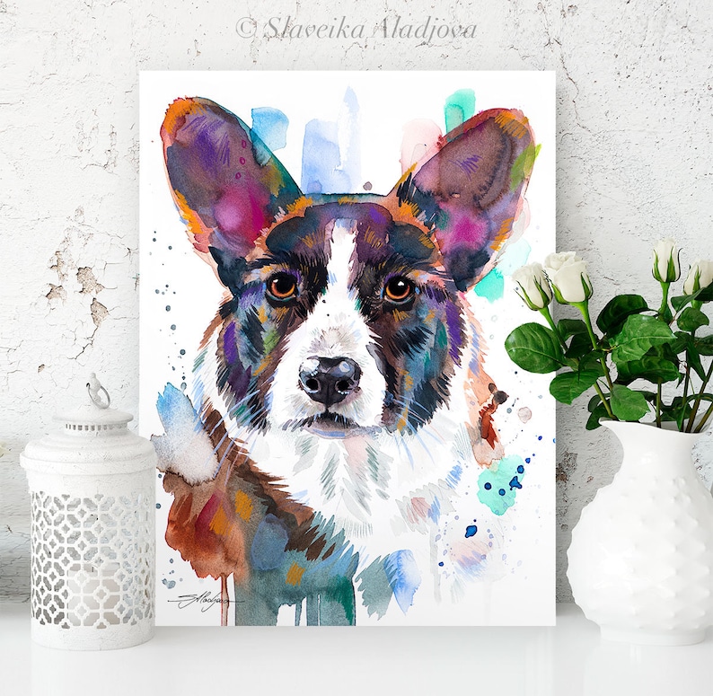 Op de afbeelding: Waterverf schilderij van een Cardigan Welsh Corgi hond met een kleurrijke achtergrond. De hond heeft bruin, zwart en wit haar en kijkt recht naar de kijker. De achtergrond is een mix van blauwe, groene en roze waterverf wassen.