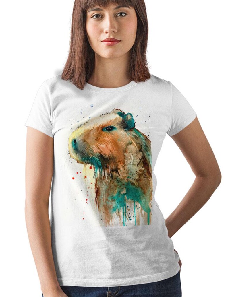 May include: A white t-shirt with a watercolor illustration of a capybara. The capybara is brown and has a teal and green watercolor effect around it.