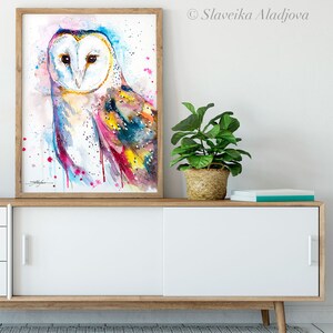 May include: A watercolor painting of a barn owl with colorful feathers. The owl is facing forward with its eyes closed. The background is a light blue with pink and white splatters.