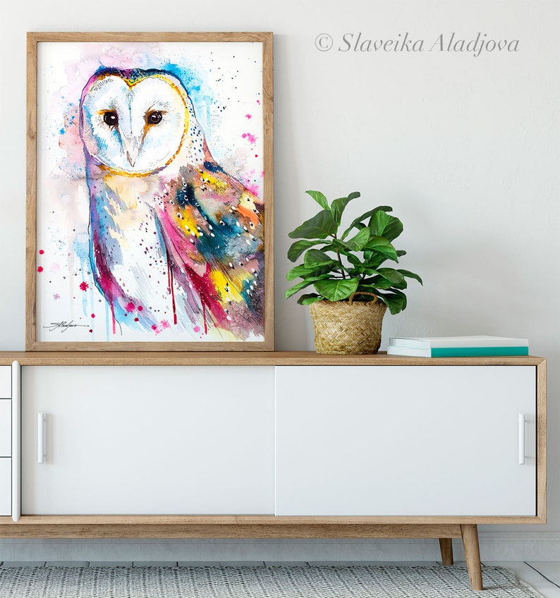 May include: A watercolor painting of a barn owl with colorful feathers. The owl is facing forward with its eyes closed. The background is a light blue with pink and white splatters.
