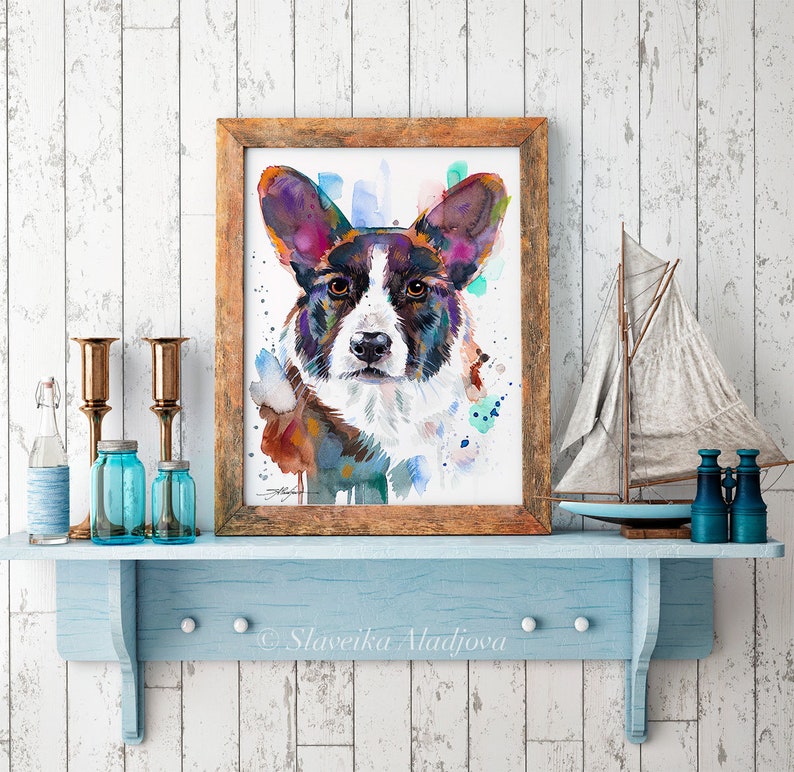 Op de afbeelding: Waterverf schilderij van een Cardigan Welsh Corgi hond met bruin, zwart en wit haar. De hond kijkt recht naar de kijker met een serieuze uitdrukking. Het schilderij is ingelijst in een rustieke houten lijst.