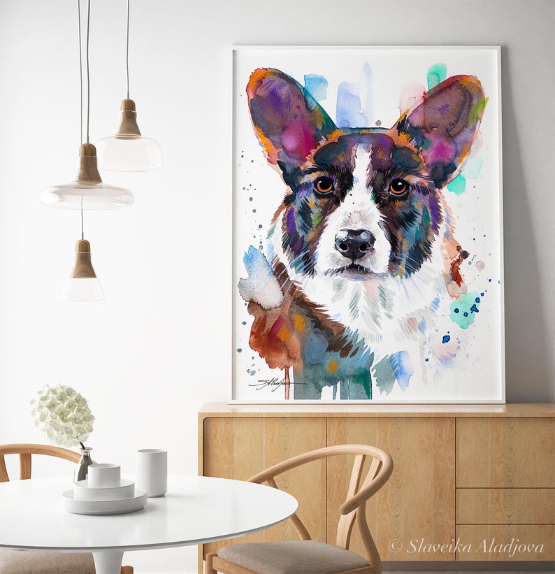 Op de afbeelding: Waterverf schilderij van een Cardigan Welsh Corgi hond met bruin, zwart en wit haar. De ogen van de hond zijn bruin en de achtergrond is een waterverf was van blauw, groen en paars.
