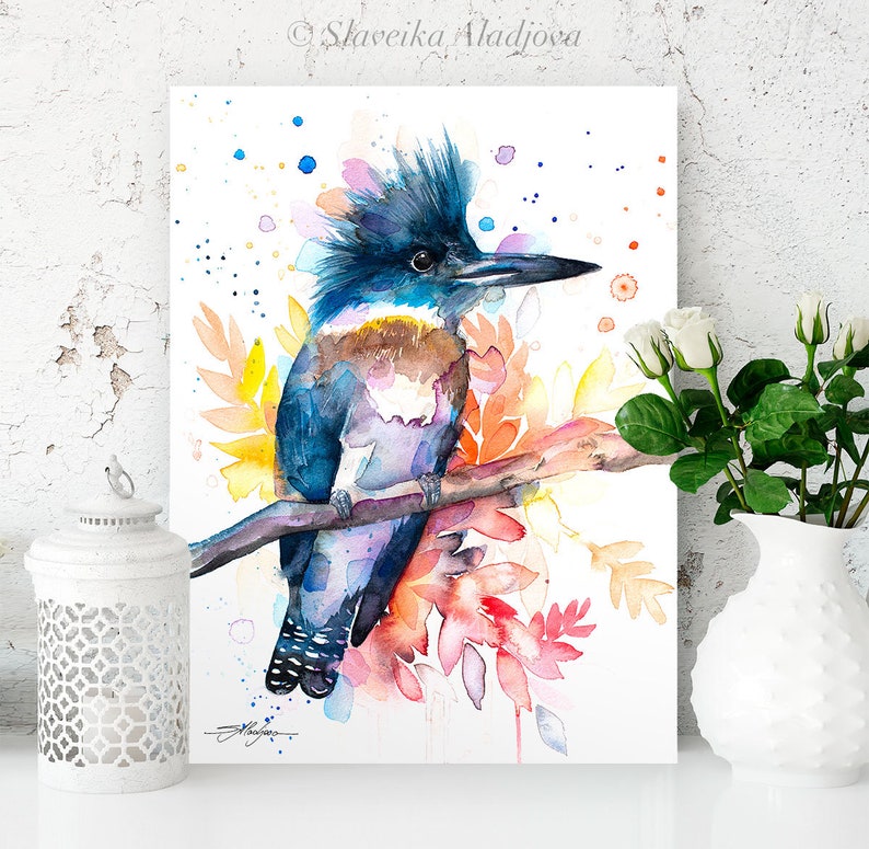 May include: Watercolor painting of a blue, purple, and brown kingfisher bird perched on a branch with colorful flowers and leaves. The background is white with watercolor splatters.