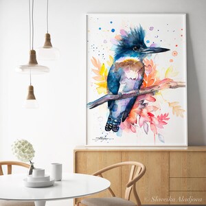May include: Watercolor painting of a blue and purple belted kingfisher perched on a branch with colorful flowers and leaves. The background is white with watercolor splatters.
