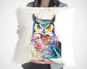 May include: A white cushion featuring a colourful watercolour painting of an owl. The owl has yellow eyes and is surrounded by splashes of blue, purple, yellow and orange paint.
