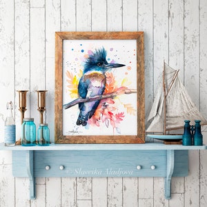 May include: Watercolor painting of a blue and purple belted kingfisher perched on a branch with colorful watercolor leaves. The bird has a crested head and a long, pointed beak. The painting is framed in a rustic wooden frame.