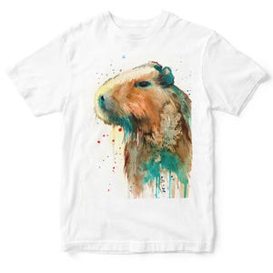 May include: A white t-shirt with a watercolor illustration of a capybara. The capybara is brown and has a light blue and green watercolor background.