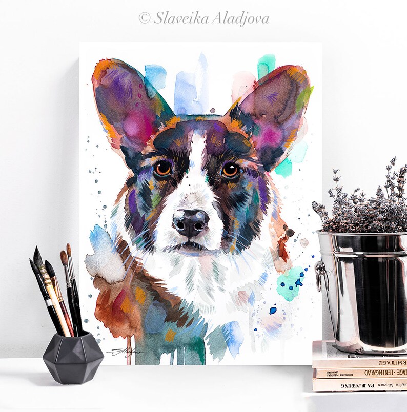 Op de afbeelding: Waterverf schilderij van een Cardigan Welsh Corgi hond met een wit en zwart gezicht en een bruin en zwart lichaam. De hond is geschilderd in een kleurrijke stijl met spatten van blauw, groen en oranje.
