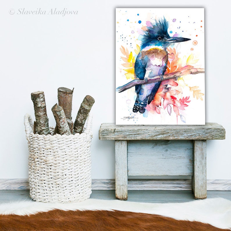May include: Watercolor painting of a blue and brown kingfisher perched on a branch with colorful flowers and leaves. The background is white with blue and orange watercolor splatters.