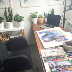 May include: A home office workspace with a wooden desk, a laptop computer, a watercolor painting of a bear, and a set of watercolor paints.