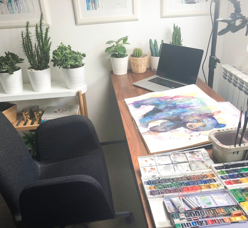 May include: A home office workspace with a wooden desk, a laptop computer, a watercolor painting of a bear, and a set of watercolor paints.