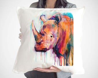 May include: A white pillow with a watercolor painting of a rhinoceros. The rhinoceros is painted in shades of orange, pink, and purple with watercolors dripping down the canvas.