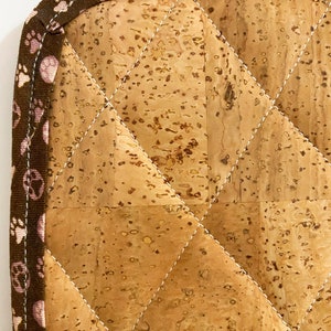 May include: A quilted cork hot pad with a brown paw print border and a beige loop for hanging. The pad features a diamond pattern created by white stitching. The cork has a natural, speckled appearance.