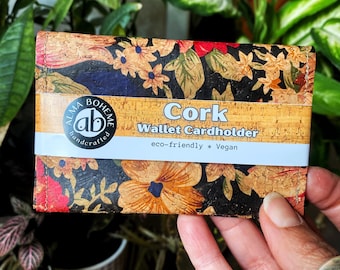 Può includere: Un portacarte in sughero con un motivo floreale rosso, arancione e giallo su sfondo nero. Il portafoglio ha una fascia bianca con le parole "Cork Wallet Cardholder" e "eco-friendly * Vegan". Il portafoglio è tenuto in mano.