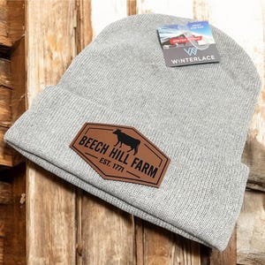 May include: Gray knit beanie with a brown leather patch that says "Beech Hill Farm - Est. 1771" and a black silhouette of a cow.
