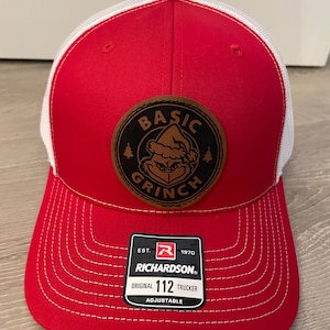 May include: Red and white trucker hat with a brown leather patch that says "Basic Grinch" and a white logo with the text "Richardson 112 Original Trucker Adjustable"