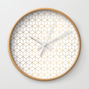 May include: A white clock with a gold geometric pattern on the face. The clock has a wooden frame.