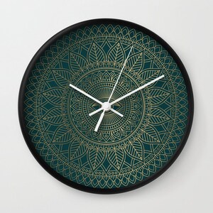 Pu&ograve; includere: Un orologio da parete rotondo con sfondo verde scuro e un design a mandala dorato. Le lancette dell'orologio sono bianche.