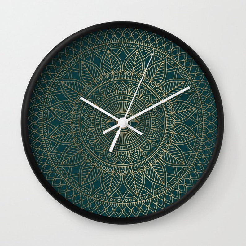 Pu&ograve; includere: Un orologio da parete rotondo con sfondo verde scuro e un design a mandala dorato. Le lancette dell'orologio sono bianche.
