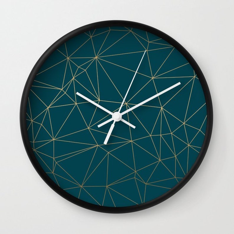 May include: A teal blue clock with a black frame and gold geometric lines. The clock hands are white.