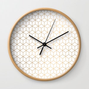 May include: A white clock with a gold geometric pattern and black hands. The clock has a wooden frame.