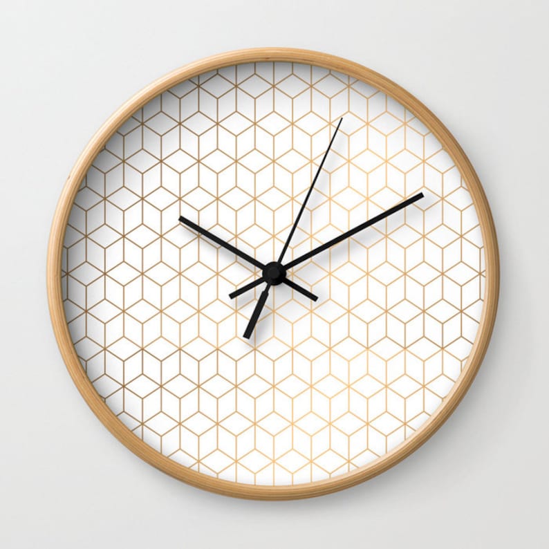 May include: A white clock with a gold geometric pattern and black hands. The clock has a wooden frame.