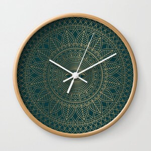 Pu&ograve; includere: Un orologio da parete rotondo con sfondo verde scuro e un design a mandala dorato. Le lancette dell'orologio sono bianche.