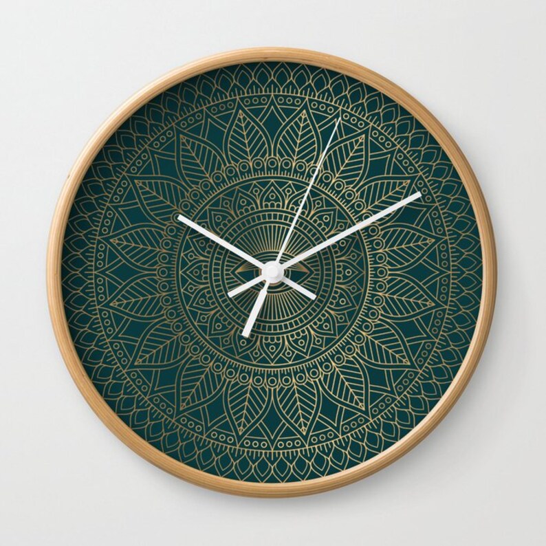 Pu&ograve; includere: Un orologio da parete rotondo con sfondo verde scuro e un design a mandala dorato. Le lancette dell'orologio sono bianche.