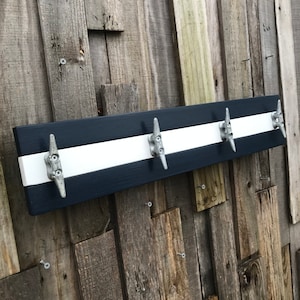 May include: A wooden coat rack with a nautical theme. It is painted navy blue and white with four silver cleat hooks.