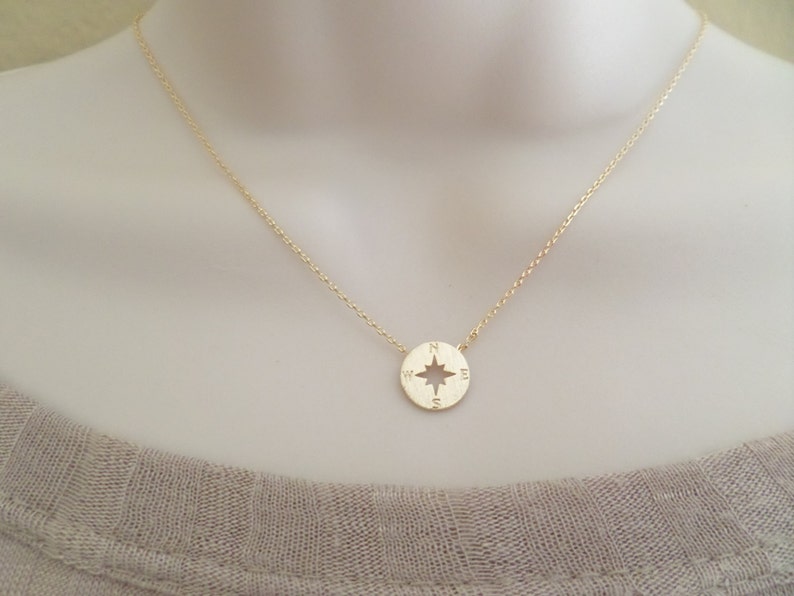 May include: A gold chain necklace with a compass pendant. The compass has a star in the center and the letters N, S, E, and W around the edge.