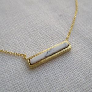 May include: A gold chain necklace with a white marble bar pendant.