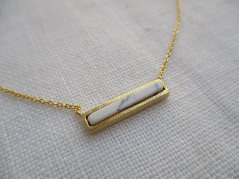 May include: A gold chain necklace with a white marble bar pendant.